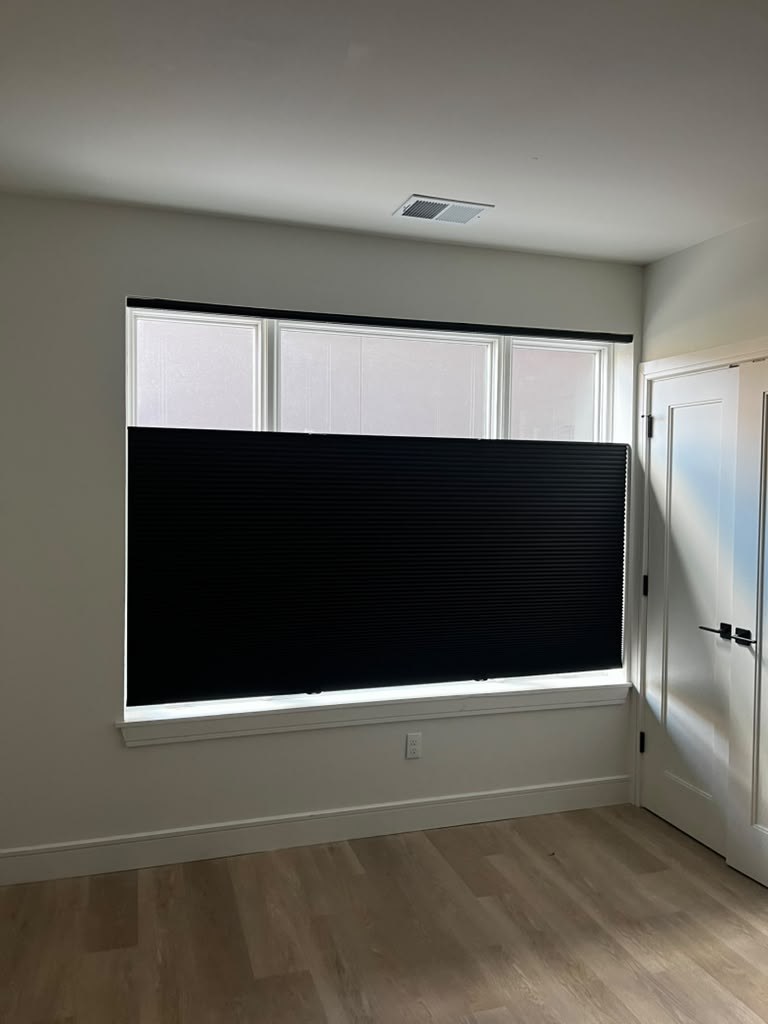 Black cellular shade partly lowered over a bedroom window